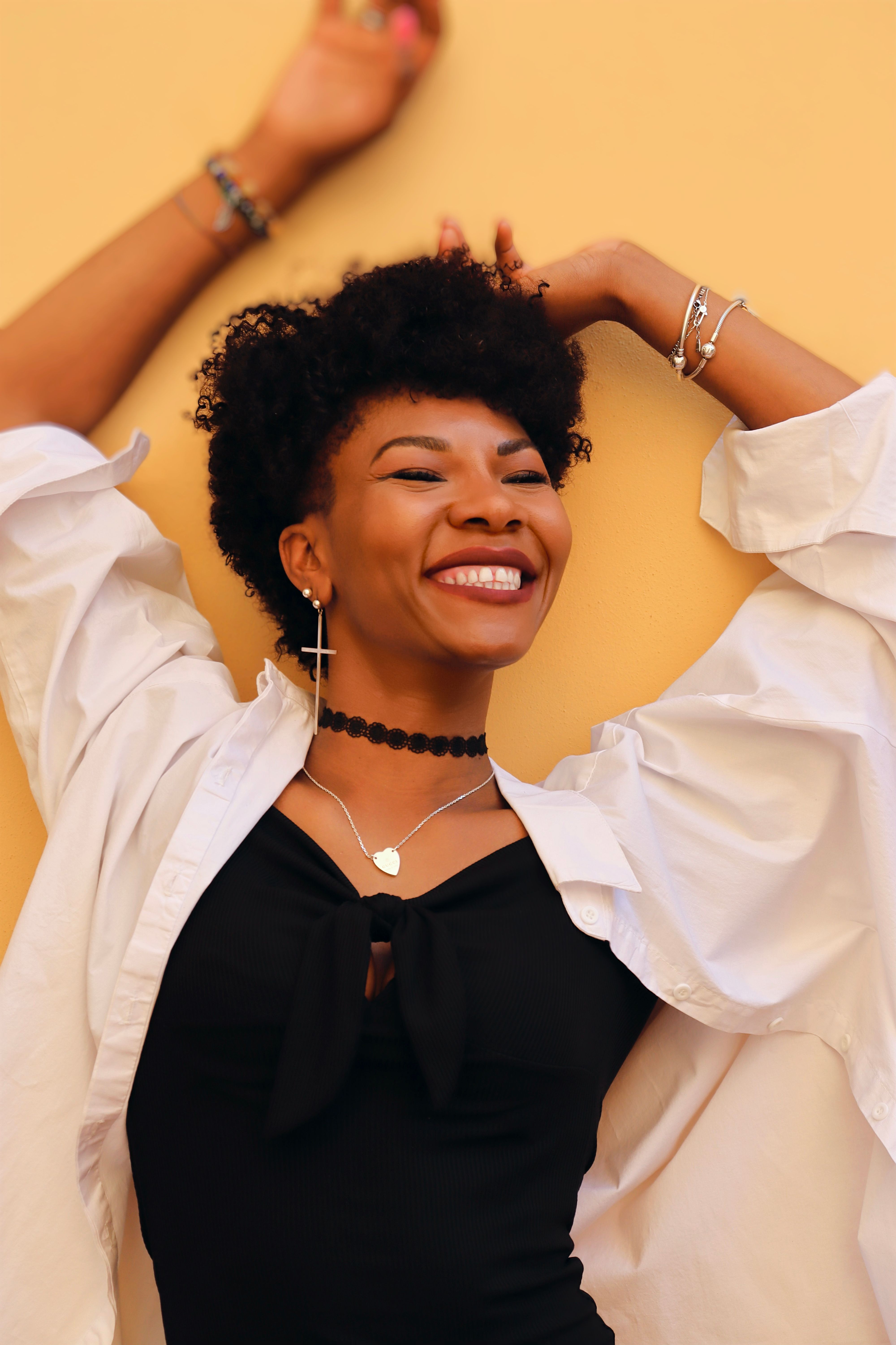 A woman standing against a warm ochre wall, arms raised, laughing